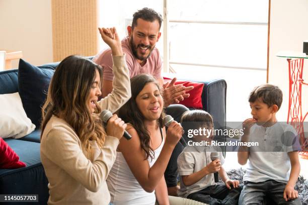 latin family singing karaoke laughing and enjoying all together in the living room of his house - family karaoke stock pictures, royalty-free photos & images