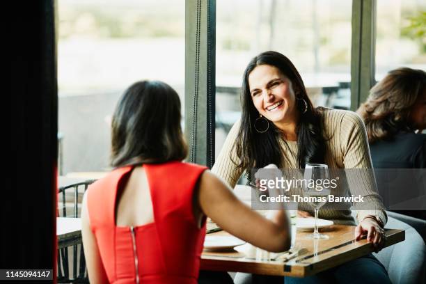 Laughing woman in discussion with friend while sharing drinks in restaurant