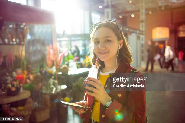 niedliches fröhliches mädchen mit smartphone musik in einem blumenladen oder einkaufszentrum hören - girl after shopping stock-fotos und bilder