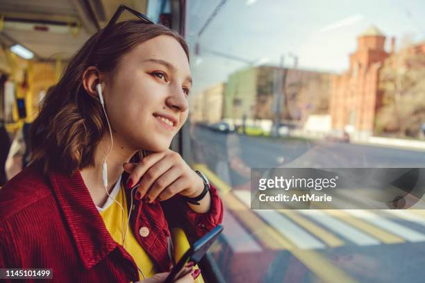 teenage girl listening to music in bus and looking out of the window - bus window stock pictures, royalty-free photos & images