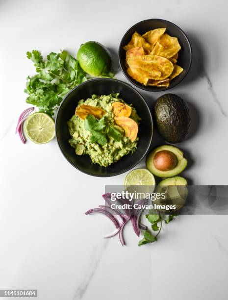 bowl of guacamole and chips with it's ingredients on a marble counter. - guacamole stock pictures, royalty-free photos & images