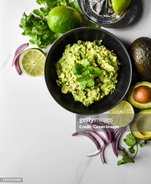 close up of bowl of guacamole and it's ingredients on a white counter. - guacamole stock pictures, royalty-free photos & images