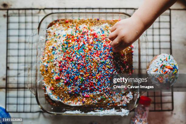 young child stealing sprinkles off of freshly baked colorful cake - hundreds and thousands stock pictures, royalty-free photos & images