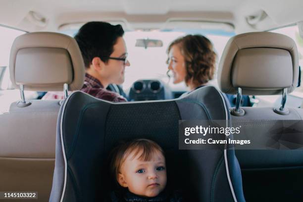 mom and dad driving in white car with baby in a car seat in the back - kid car seat stock-fotos und bilder