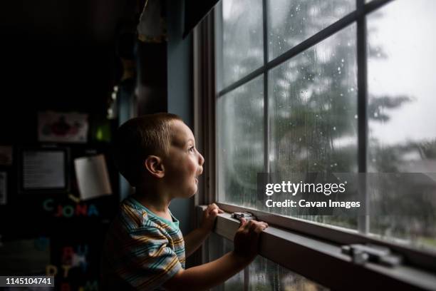 excited boy looking out a window with raindrops at a stormy sky - summer storm stock pictures, royalty-free photos & images