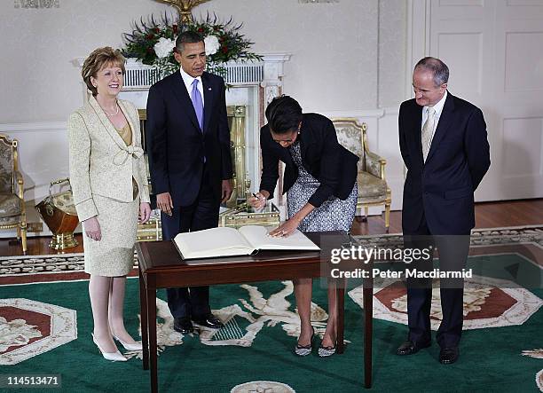 President Barack Obama watches as First Lady Michelle Obama signs a visitors book as President of Ireland Mary McAleese and Dr. Martin McAleese look...