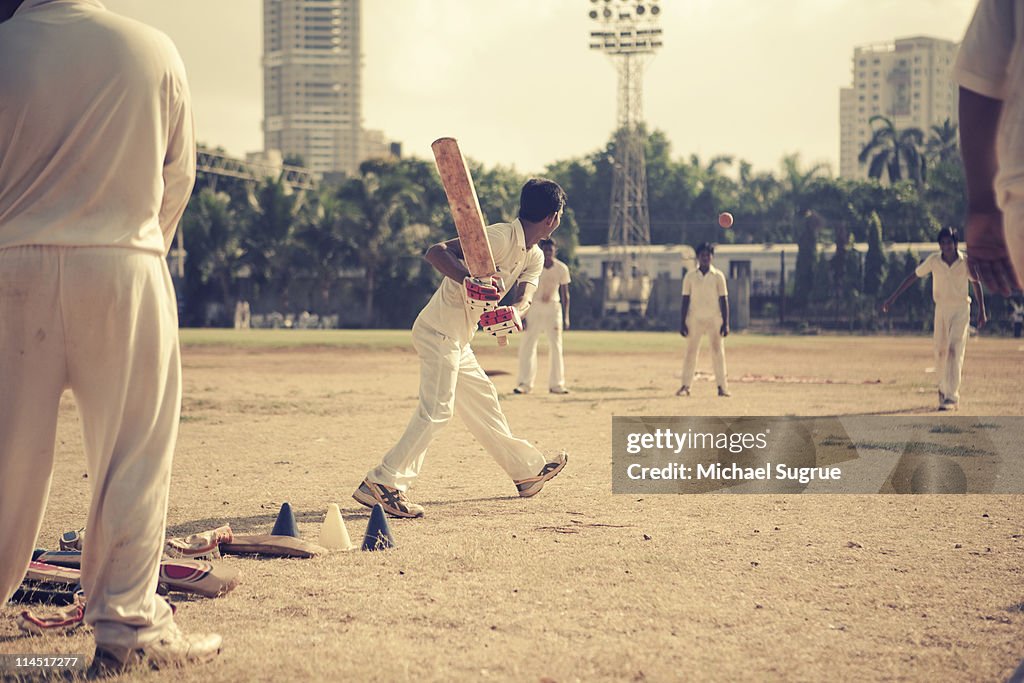 Youths play cricket in an open field in India.