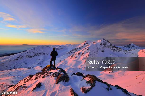 man standing on top of a snowcapped mountain at sunrise - alpenglow - fotografias e filmes do acervo