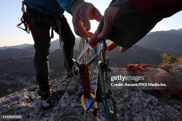 low angle view of climbers exchanging gear on rock summit at sunset - カラ�ビナ ストックフォトと画像