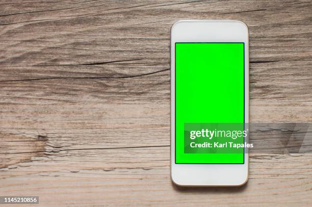 a mobile phone with green screen on a wooden table - smartphone background stockfoto's en -beelden