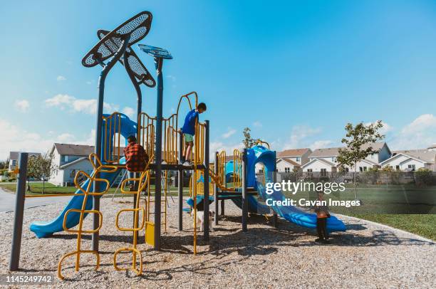 brothers playing on outdoor play equipment at playground during sunny day - speeltuintoestellen stockfoto's en -beelden