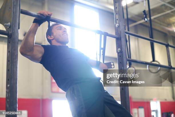 Confident male adaptive athlete screaming while doing chin-ups in gym