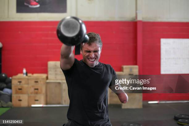 Male adaptive athlete lifting kettlebell while standing against wall in gym