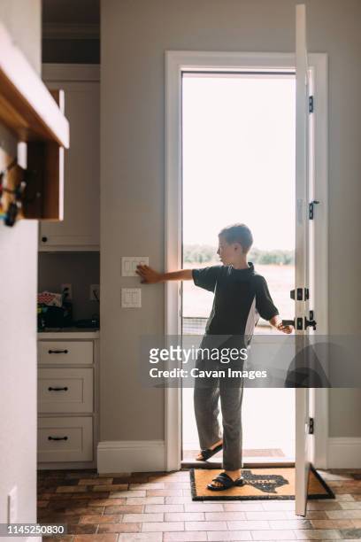 full length of boy pressing light switch while standing at doorway in house - electrical switch stock-fotos und bilder