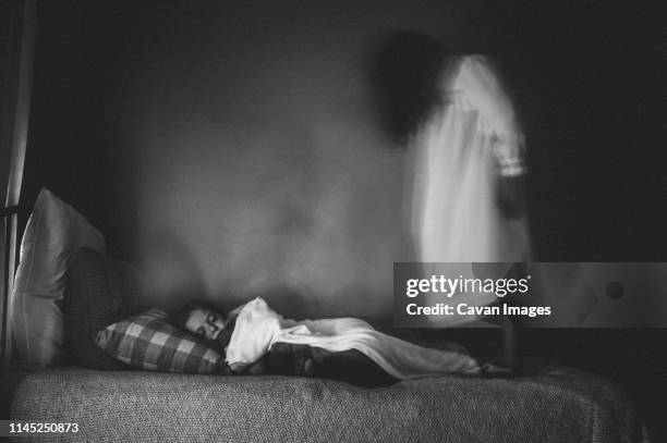 side view of spooky girl standing by sleeping sister on bed against wall at home - fantasma fotografías e imágenes de stock