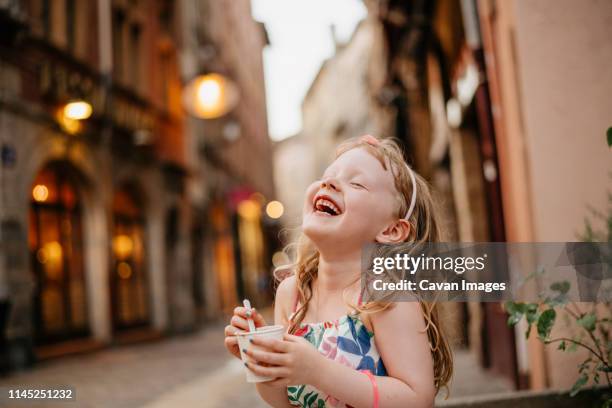 happy girl eating food while standing on street against buildings in city during sunset - lyon food stock pictures, royalty-free photos & images