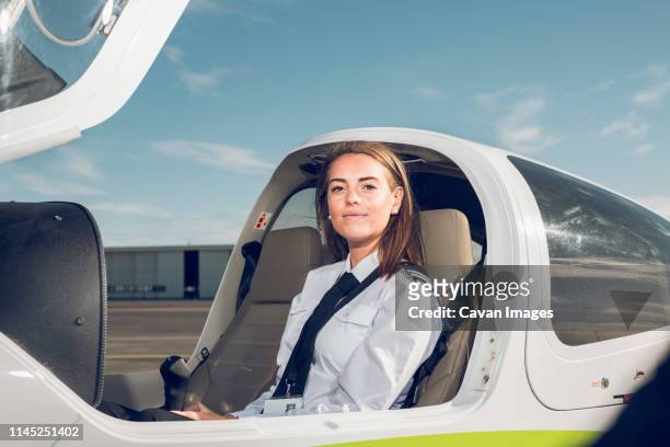 portrait of confident female pilot sitting in airplane against blue sky at airport - aviatrice stock pictures, royalty-free photos & images