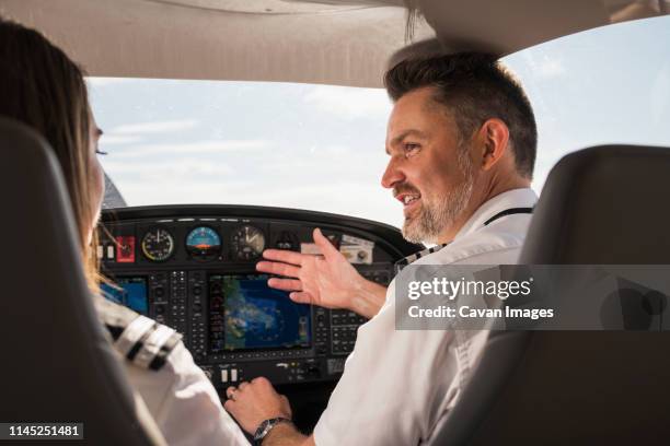 rear view of male pilot teaching female trainee to operate control panel in airplane at airport - pilotar fotografías e imágenes de stock