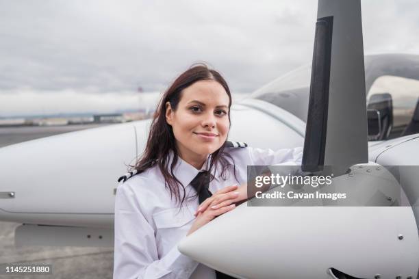 portrait of smiling female pilot standing by airplane on airport runway against cloudy sky - pilot fotografías e imágenes de stock