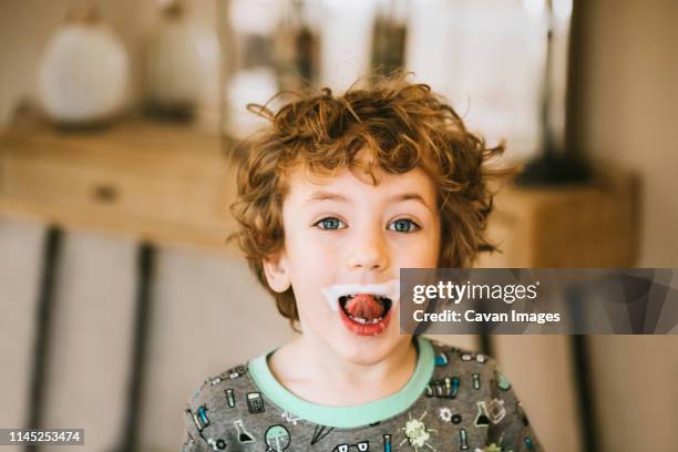 portrait of cute boy with milk mustache sticking out tongue at home - milk moustache stock pictures, royalty-free photos & images