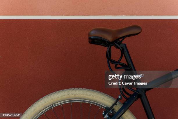 cropped image of bicycle parked by brown wall in city - fahrradsattel stock-fotos und bilder