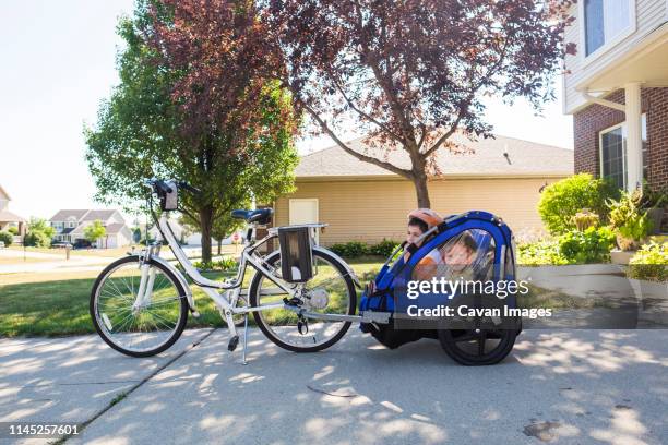 brothers sitting in bike trailer on footpath - cycle stock-fotos und bilder