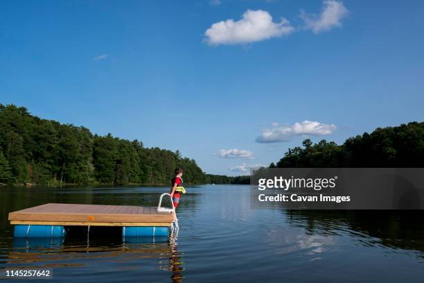 side view of boy standing on floating platform in lake at forest against sky - floß stock-fotos und bilder