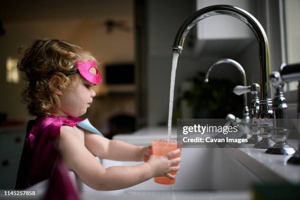 side view of girl wearing superhero costume filling water in drinking glass while standing at home - kitchen sink running water stock pictures, royalty-free photos & images