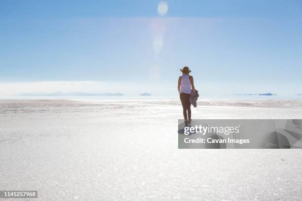 rear view of woman walking on bonneville salt flats against blue sky during sunny day - bonneville salt flats stockfoto's en -beelden