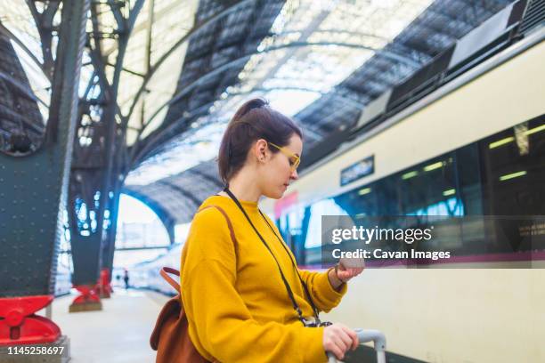 side view of woman with luggage checking time while standing at railroad station platform - auf die uhr sehen stock-fotos und bilder