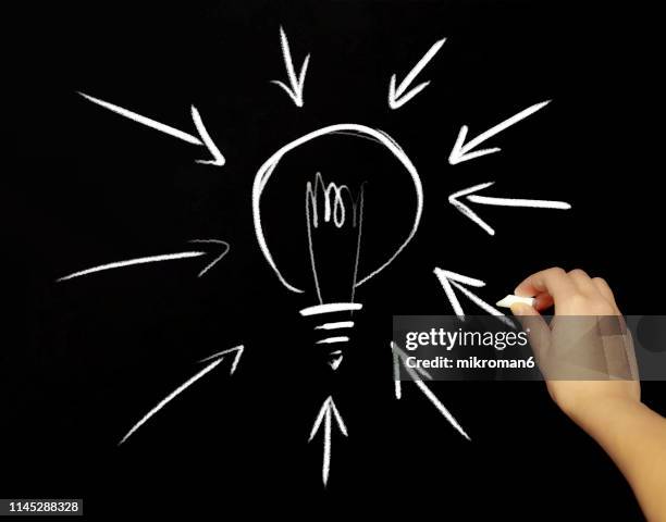 hand drawing a light bulb with chalk in black board - hand drawn arrow stock-fotos und bilder