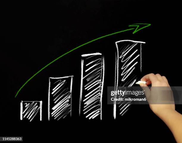 hand drawing a graph with chalk in black board - chalk arrow stock-fotos und bilder