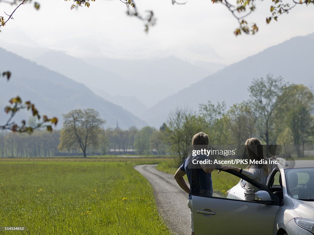 Couple look down meadow road toward mountains