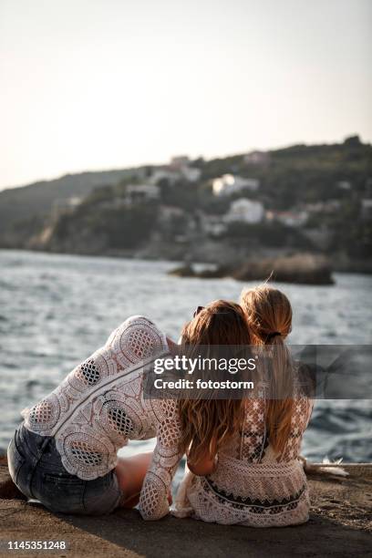 vrouwelijke vrienden zittend aan de zee, genieten van het uitzicht - long hair stockfoto's en -beelden