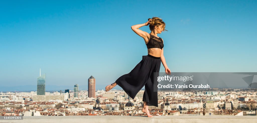 Young blond modern dancer dancing in the streets of Lyon, France with a panorama of the city in background
