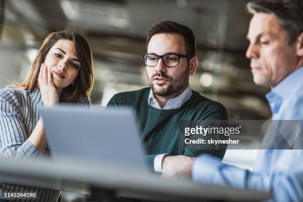 junges ehepaar und immobilienmakler mit laptop auf einem treffen im büro. - mid adult stock-fotos und bilder