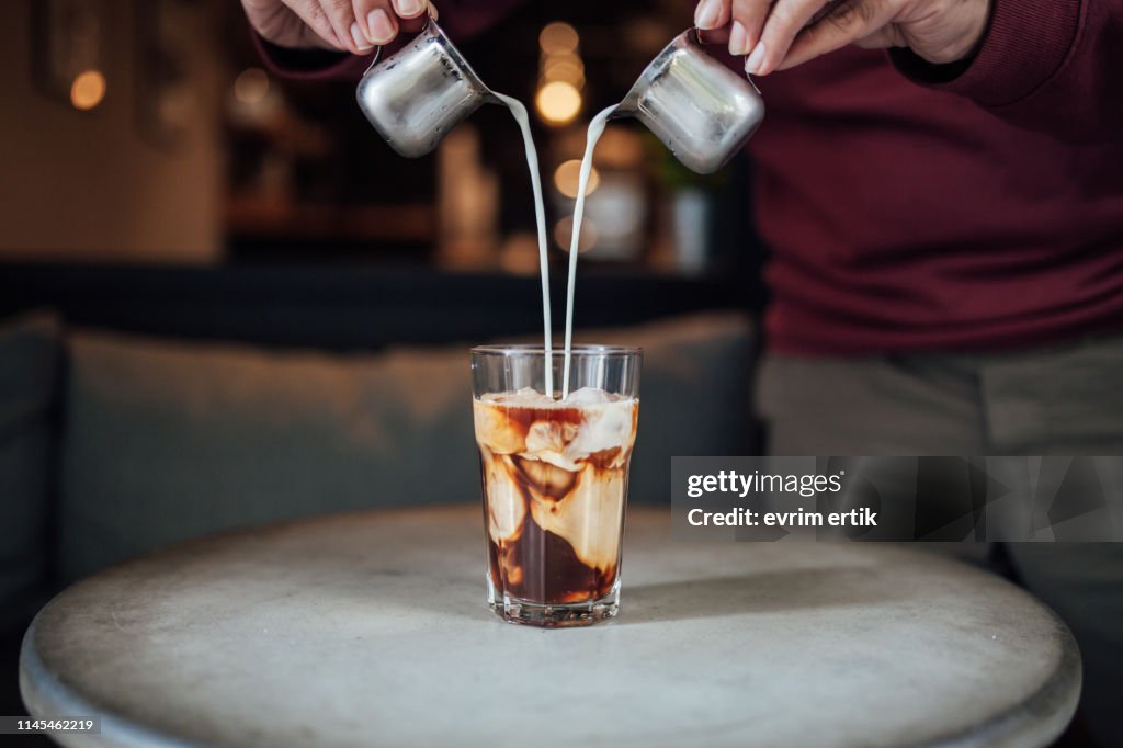 Man gießt Milch in Eiskaffee