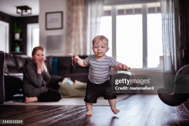 parents watching and helping baby son take first steps at home - primeiros passos imagens e fotografias de stock