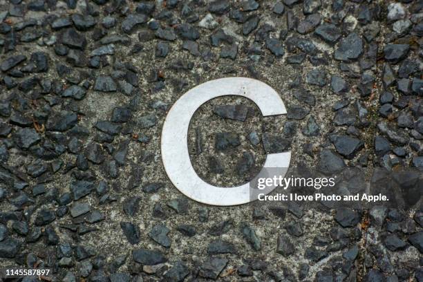 a small letter of the metal alphabet embedded in a road - letter c stock pictures, royalty-free photos & images