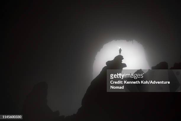 a caver stands on the 'hand of dog' stalagmite, backlit by the 1st doline, inside the world largest cave in vietnam - spelunking stockfoto's en -beelden