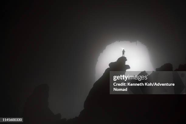 a caver stands on the 'hand of dog' stalagmite, backlit by the 1st doline, inside the world largest cave in vietnam - spelunking stock pictures, royalty-free photos & images