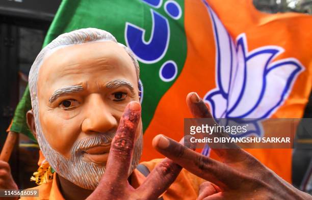 An Indian supporter of Bharatiya Janata Party wearing a mask of Prime Minister Narendra Modi flahes the victory sign as he celebrates on the vote...
