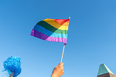 LOW ANGLE VIEW OF HAND HOLDING rainbow flag AGAINST SKY