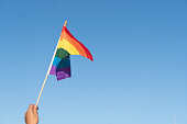 LOW ANGLE VIEW OF HAND HOLDING rainbow flag AGAINST SKY