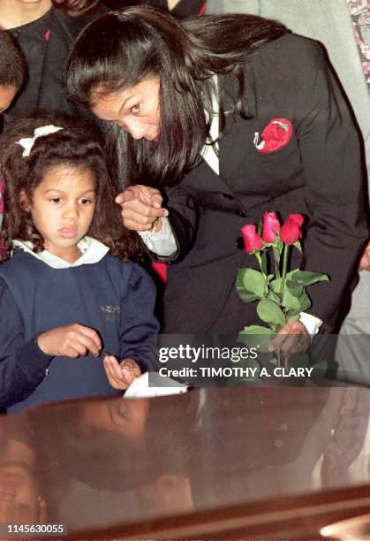 Jeanne Ashe, wife of the late Arthur Ashe, points out to daughter Camera as the casket of Ashe is lowered into the ground 10 February 1993 during...