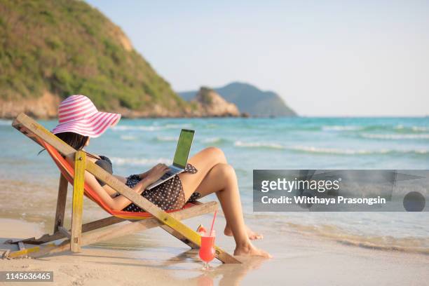 young attractive woman in dress, sunglasses and hat, working in laptop on the beach - time off work stock pictures, royalty-free photos & images