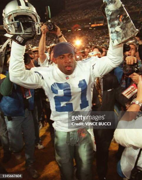 Dallas Cowboys cornerback Deion Sanders hoists the Vince Lombardi Super Bowl trophy as he walks off the field to the locker room after defeating the...