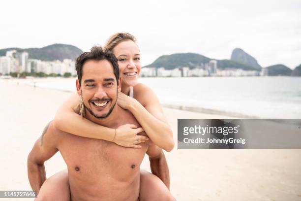 portrait of cheerful man carrying girlfriend on beach - copacabana stock pictures, royalty-free photos & images
