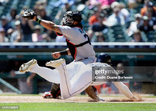 Niko Goodrum of the Detroit Tigers dives at home plate to score against catcher Jorge Alfaro of the Miami Marlins on a sacrifice fly hit by Ronny...