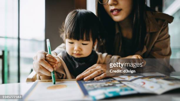 young mother holding hand of cute little daughter colouring and writing together joyfully - kid holding crayons stock pictures, royalty-free photos & images